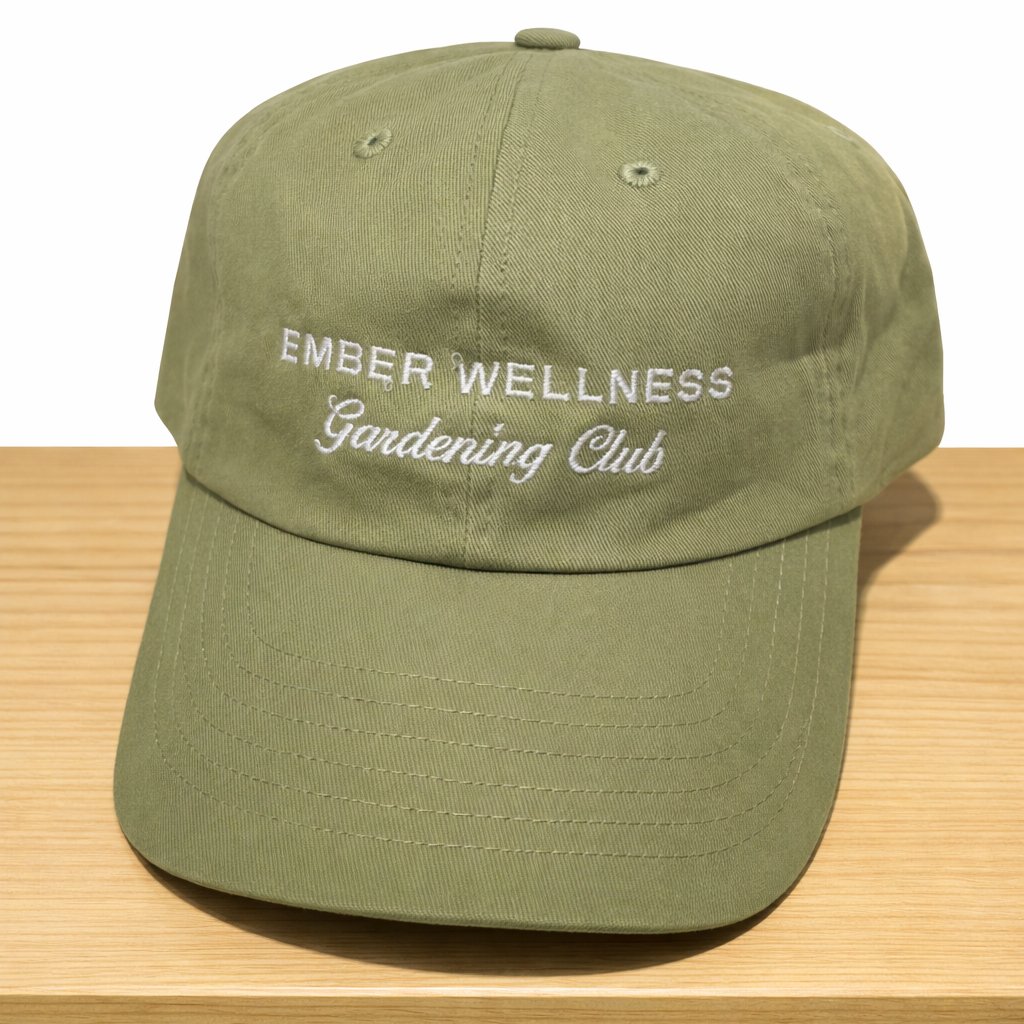 Green cap with 'Ember Wellness Gardening Club' text on a wooden surface