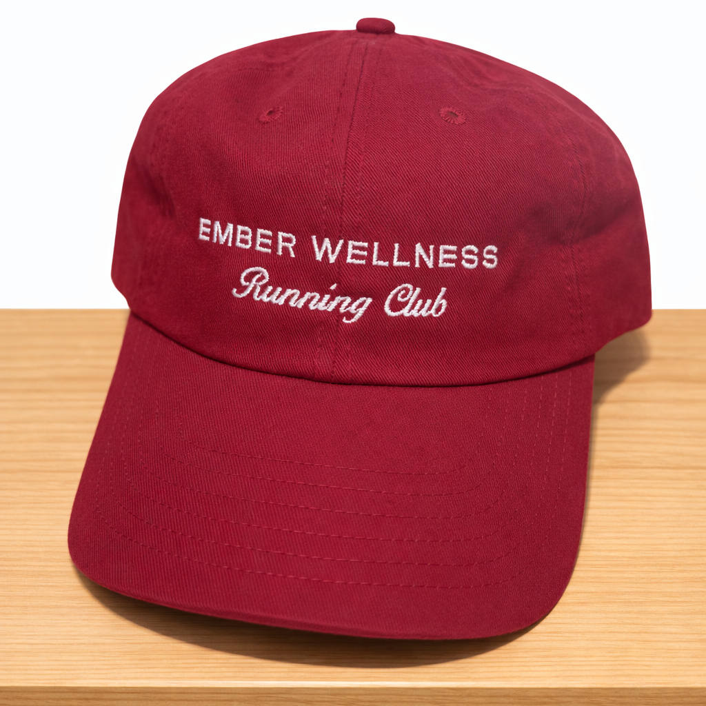 Red cap with 'Ember Wellness Running Club' text on a wooden surface