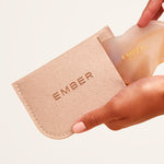 Our patented Cloud Gua Sha tool designed to hug every curve on the body, seen here in agate and slipping into our soft felt Ember travel pouch.
