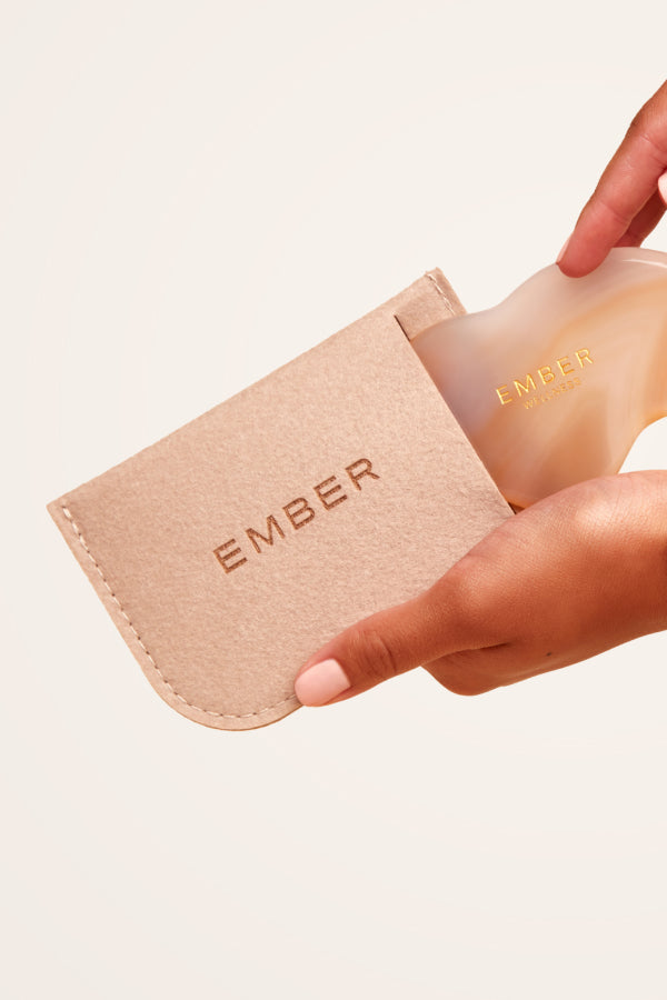 Our patented Cloud Gua Sha tool designed to hug every curve on the body, seen here in agate and slipping into our soft felt Ember travel pouch.