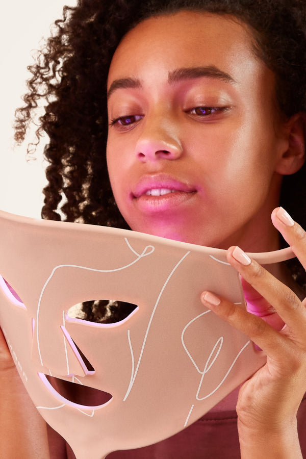 Ember Wellness's Rejuvenating Light Therapy Mask in pink being held by woman.
