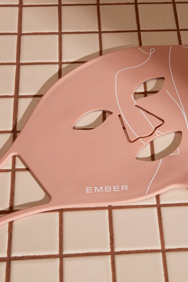 Ember Wellness' Rejuvenating Light Therapy Mask in pink rests on a tile surface.